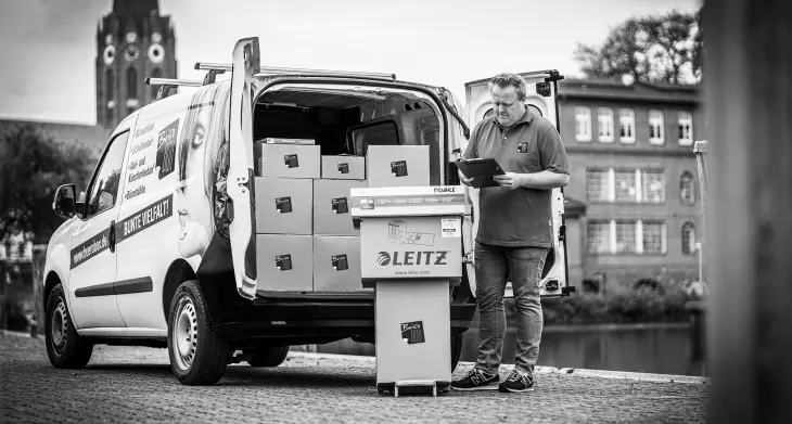 Ein Mann steht vor einem geöffneten Lieferwagen und liefert Pakete aus.