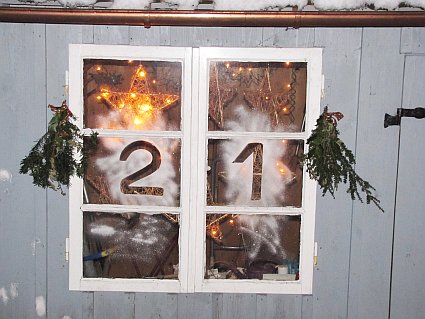Beleuchtetes Adventsfenster mit der Zahl 21 und Tannenzweigen als Deko.
