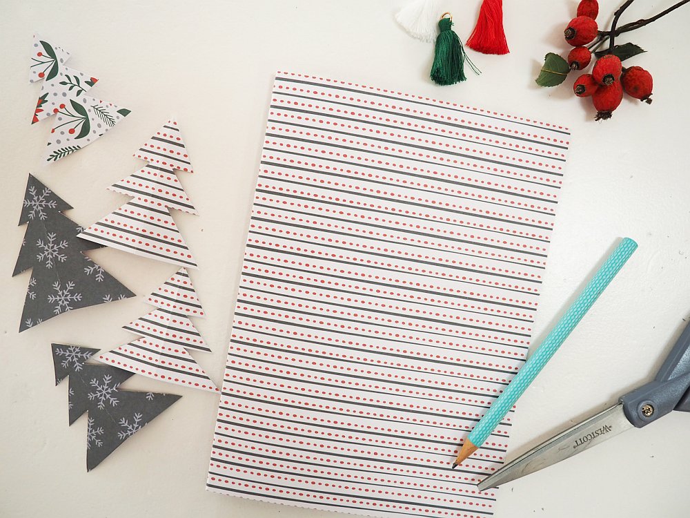 Weihnachtliches Bastelpapier mit Muster, umgeben von Papierbäumen und Deko.