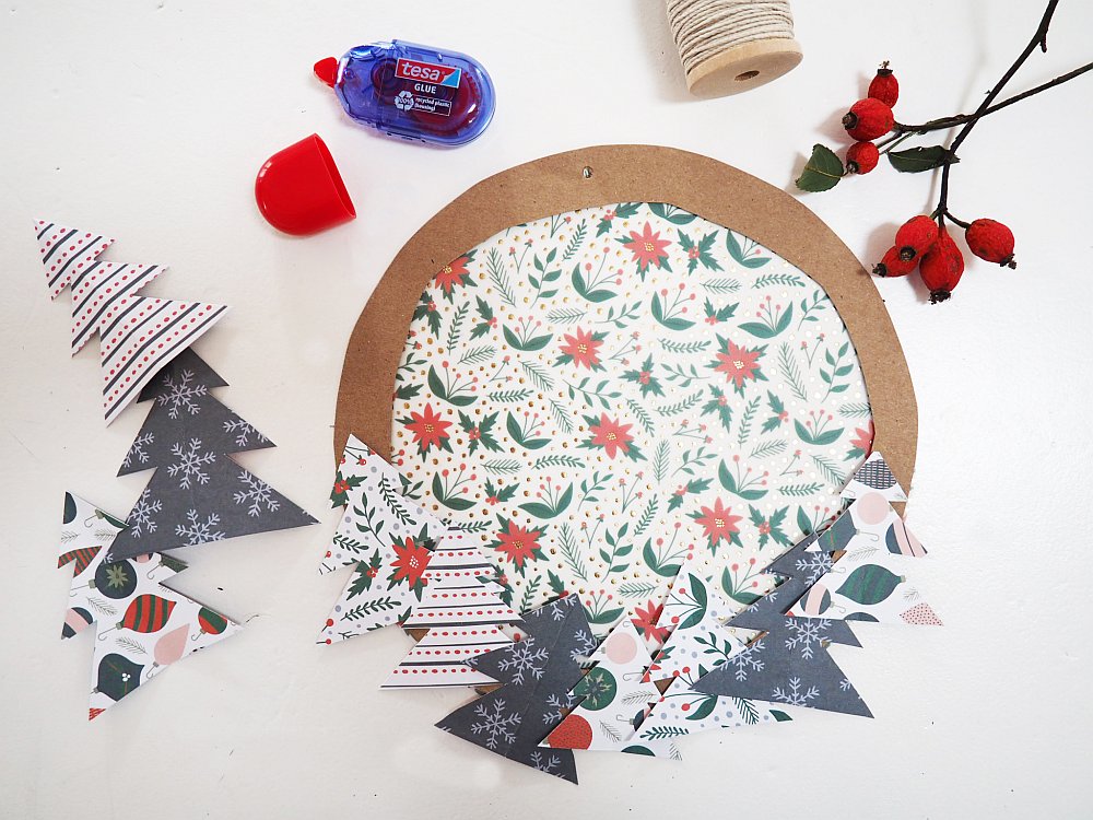 Weihnachtskranz aus Papier mit Deko-Tannenbäumen und Bastelmaterial.