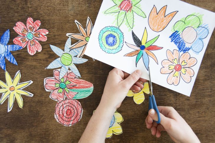 Jemand schneidet bunt gemalte Blumen aus einem Blatt Papier aus.