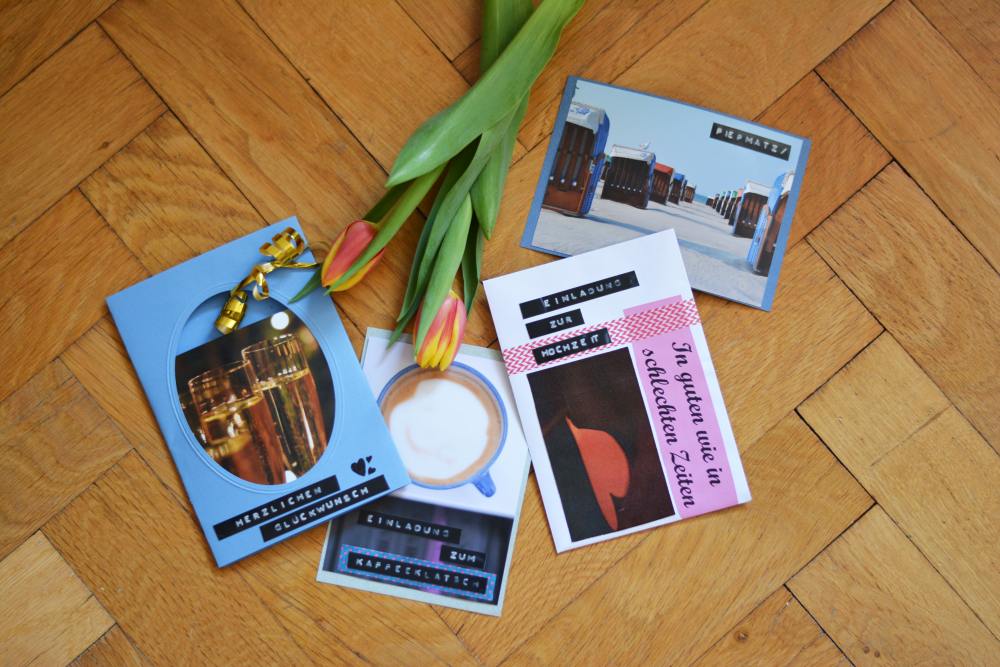 Auf einem Parkettboden aus Holz liegen verschiedene DIY-Karten, die mit Prägeband von Dymo verziert wurden. Vom oberen Bildrand ragt eine Tulpe ins Bild. 