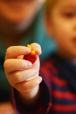 Nahaufnahme einer Kinderhand, die eine rot-gelb geformte Maus aus Knetbienenwachs in die Kamera hält.