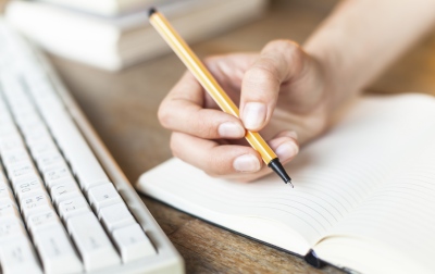  Hand schreibt mit Fineliner in ein aufgeschlagenes Notizbuch.