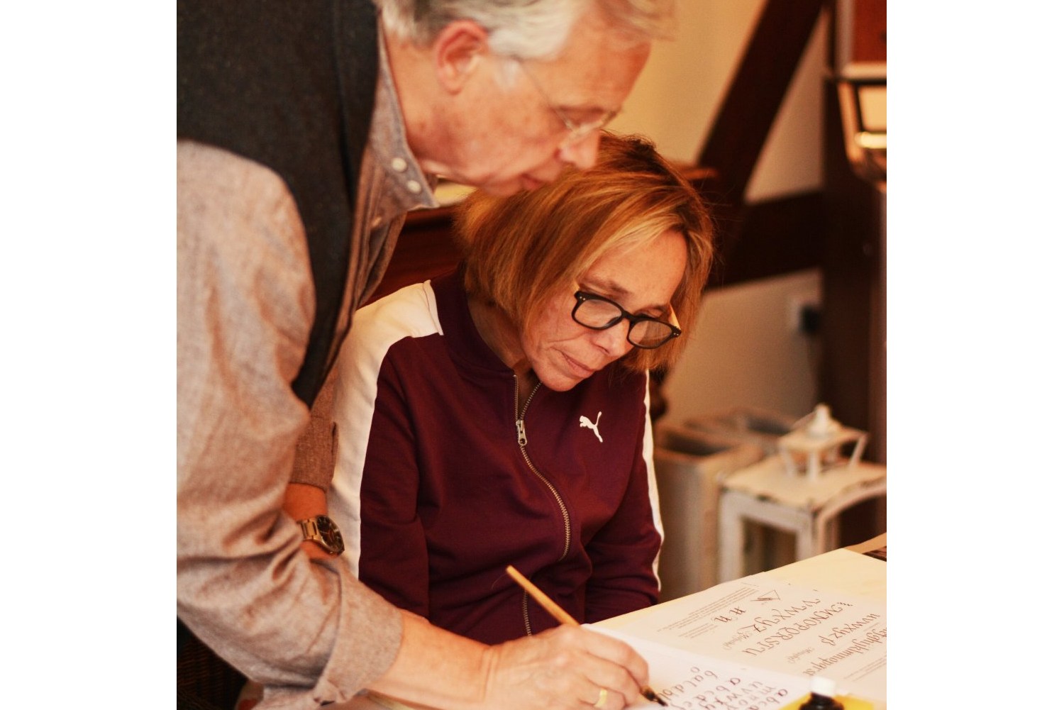 Martin Heickmann steht neben einer Teilnehmerin des Workshops und zeigt ihr, wie man kalligrafiert.