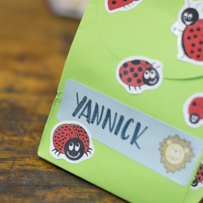 Eine grüne Geschenktüte wurde mit einigen Marienkäfer-Stickern von Avery Zweckform beklebt. Außerdem ist ein Etikett mit einem Löwenkopf auf die Tüte geklebt worden. Auf diesem ist der Name "Yannick" gelettert.