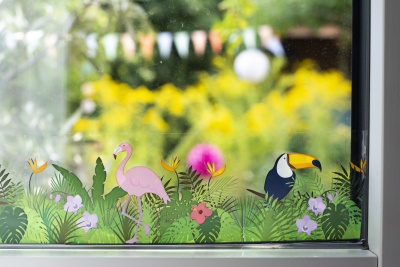 Ein Fenster, welchen mit einem Washitape mit Dschungel-Motiv beklebt wurde. Durch das Fenster sieht man verschwommen einen Garten mit gelben Blumen.