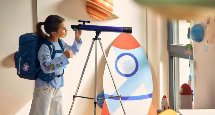 Ein Mädchen mit einem Schulranzen von ergobag auf dem Rücken blickt durch ein Fernrohr