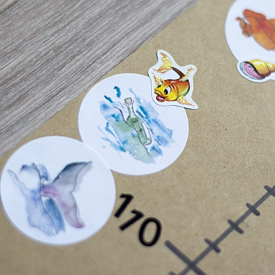 Nahaufnahme bunter Sticker mit Fisch, Flaschenpost und Flosse.