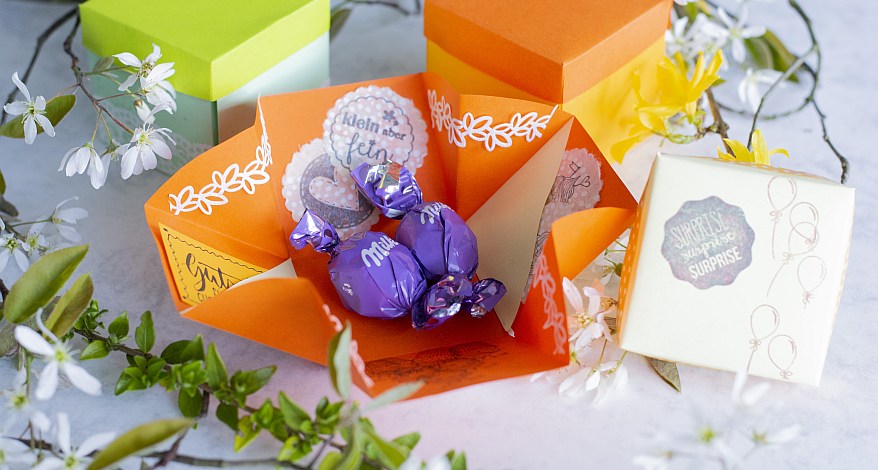 Bunte Explosionsbox mit Pralinen und liebevoller Verzierung.