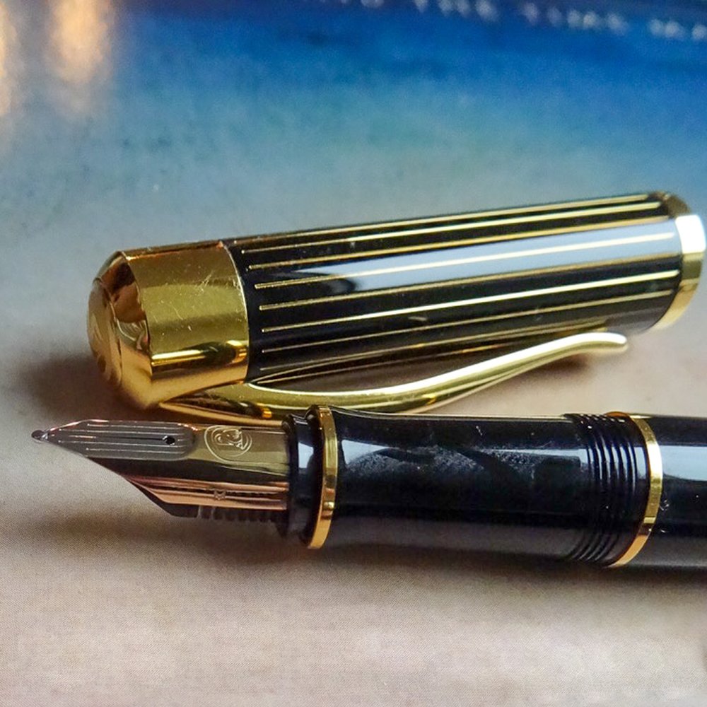 Eine nahaufnahme des Pelikan Duktus in schwar/gold. Die Füllerkappe ist schwarz glänzend und besitzt einen goldenen Clip sowie goldene Streifen. Der Griff des Füllers ist mit goldenen Verzierungen geschmückt. Der Füller hat eine Goldfeder.