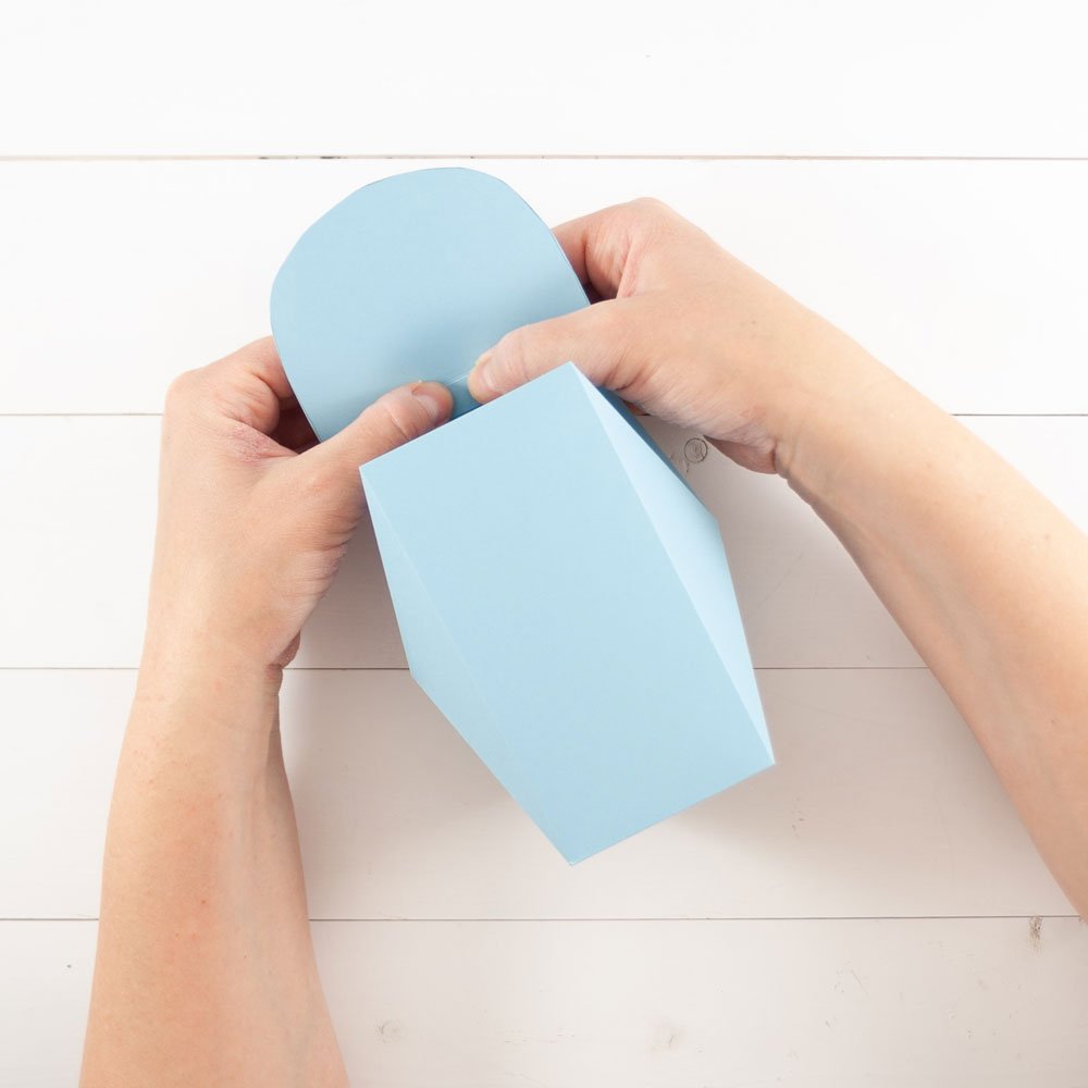 Zwei Hände kleben eine ausgeschnittene Schachtel zusammen.