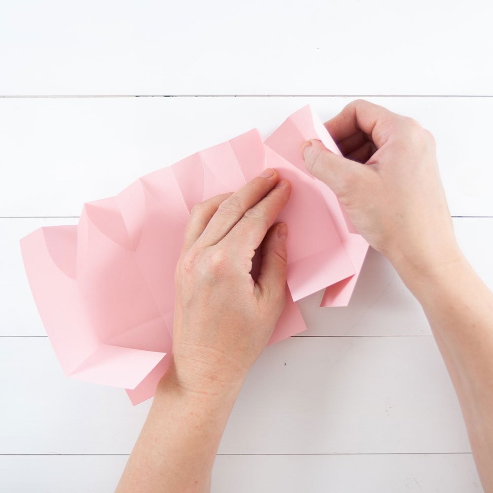 Zwei Hände knicken ein rosa Papier an Falzungen. 