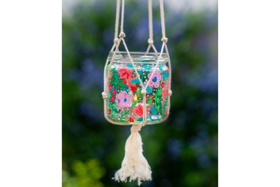 Ein bunt gestaltetes Windlicht hängt in Makramee-Aufhängung