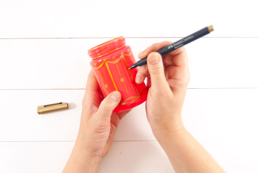 Ein rot besprühtes Glas wird mit goldenen Ornamenten bemalt