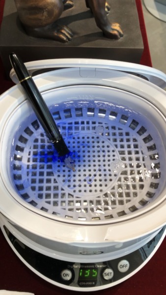 Eingeschalteter Reiniger mit einem Füller drin. Das Wasser ist blau gefärbt.