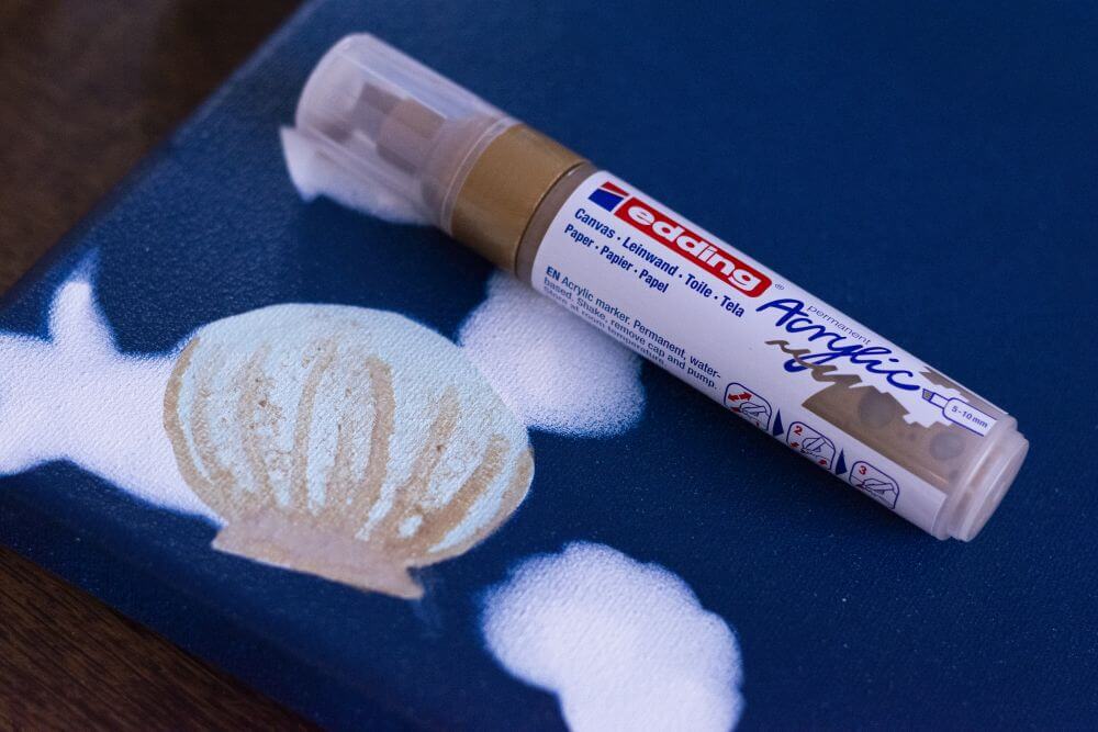 Nahaufnahme einer Muschel, die mit Acryl auf Leinwand gemalt wurde. Daneben liegt ein Acrylmarker von Edding in gold.