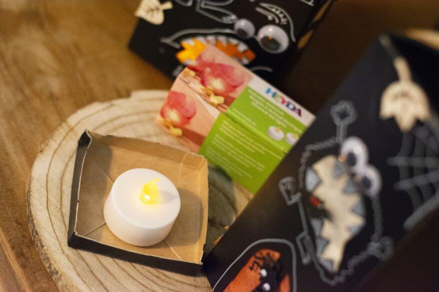 Detailaufnahme einer Do it yourself-Dekoidee zu Halloween: Ein elektrisches Teelicht steht im Boden eines selbstgemachten Gruselhauses aus einem leeren Milchkarton.