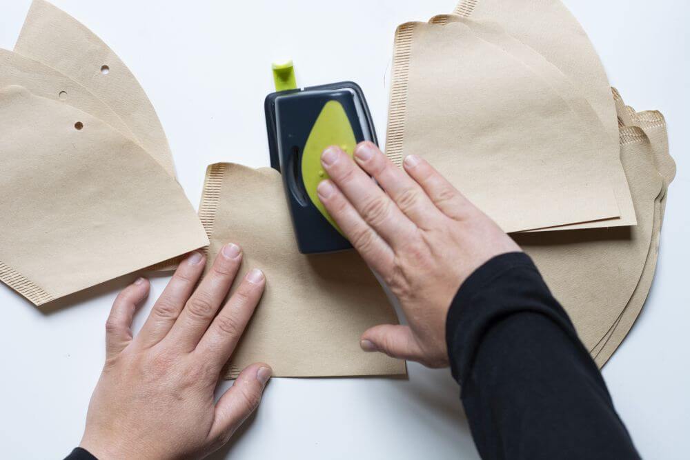 Mit Hilfe eines Lochers werden Löcher an die Oberseite von zahlreichen Kaffeefiltern gestanzt.