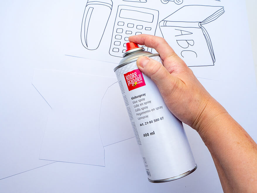 Jemand möchte Foto-Props für die Einschulung basteln und sprüht dafür ein Papier mit Sprühkleber von Knorr-Prandell ein. Der Untergrund ist weiß. Foto: Johanna Rundel