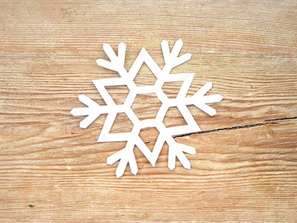 Auf einem rustikalen, hellen Holzbrett liegt eine aus weißem Papier von Artoz ausgeschnittene Schneeflocke. Foto: Johanna Rundel