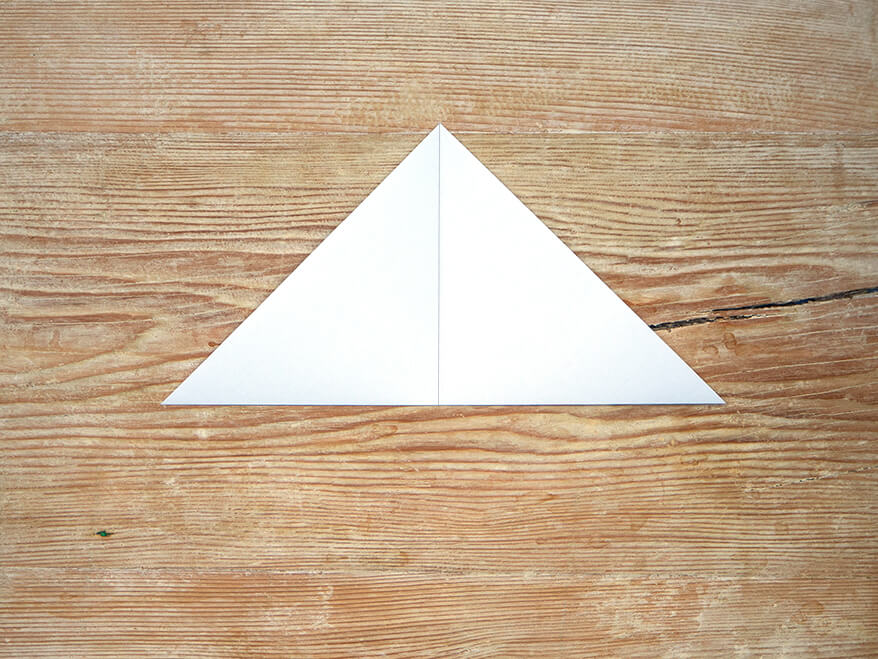 Ein zu einem Dreieck gefaltetes, quadratisches Blatt Papier der Marke Artoz. Der Untergrund ist ein rustikales, helles Holzbrett. Foto: Johanna Rundel