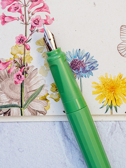 Auf einem Bogen Briefpapier mit buntem Blumenmuster von Rössler liegt ein hellgrüner Füller. Foto: Johanna Rundel