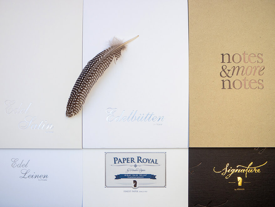 Sechs verschiedene Schreibblöcke von Rössler wurden dicht an dicht, neben und übereinander arrangiert, so dass sie die gesamte Fläche des Bildes bedecken. In der linken oberen Hälfte liegt eine schwarz-weiße Feder. Foto: Johanna Rundel