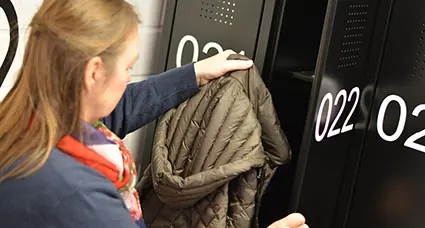 Blick über die Schulter einer Frau, die gerade ihre Jacke in einen Spind hängt.
