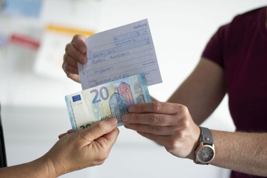 Eine Hand nimmt einen 20-Euro-Schein entgegen und bekommt dafür eine handschriftliche Quittung entgegengestreckt. 