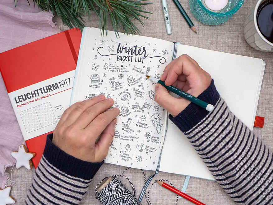 Jemand schreibt mit einem dunkelgrünen Drehgriffel von LEUCHTTURM1917 eine Winter-Bucket-Liste in ein Bullet Journal. Foto: Johanna Rundel