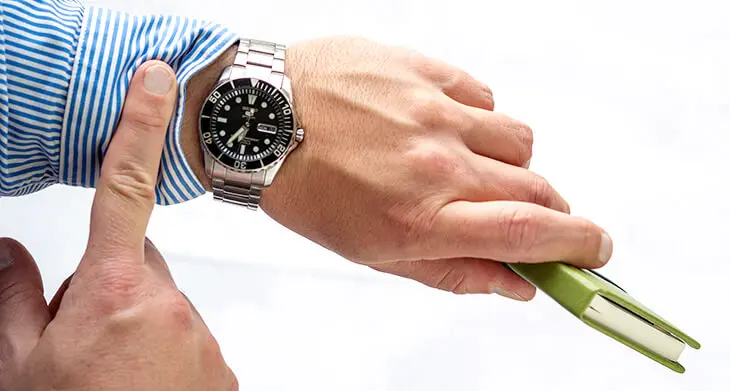 Eine Person im blau-weiß gestreiften Hemd hält den Arm mit einer Armbanduhr ins Bild. Sie hält einen Planer von Athesia. Mit der anderen Hand zieht sie die Manschette hoch. Foto: Johanna Rundel