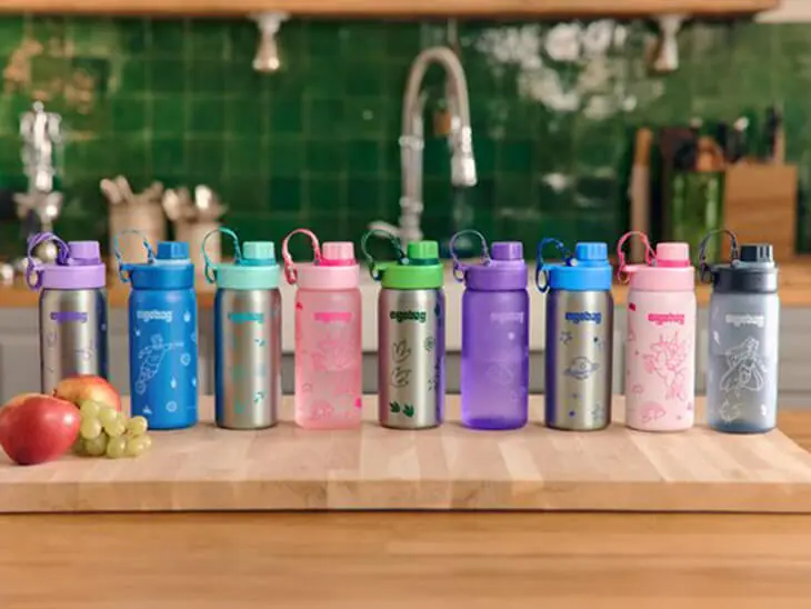 Verschiedene Trinkflaschen von ergobag stehen nebeneinander auf einem Küchenblock aus Holz.)