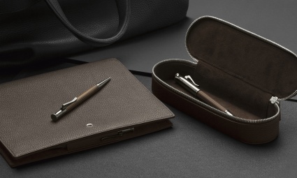 2 Kugelschreiber von Graf von Faber-Castell liegen in einem braunen Leder-Etui und auf einer braunen Dokumentenmappe von Graf von Faber-Castell.