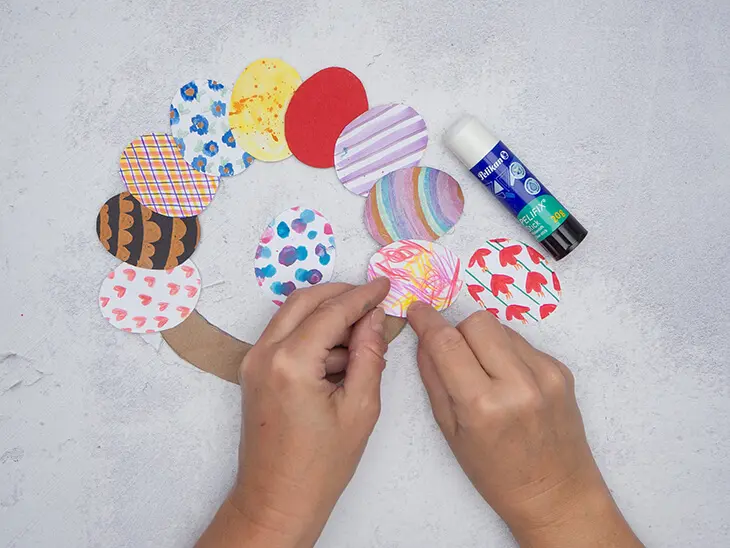 Jemand klebt mit einem Klebestift von Pelikan buntbemalte Papiereier auf einen Pappring, um einen Osterkranz zu basteln. Foto: Johanna Rundel