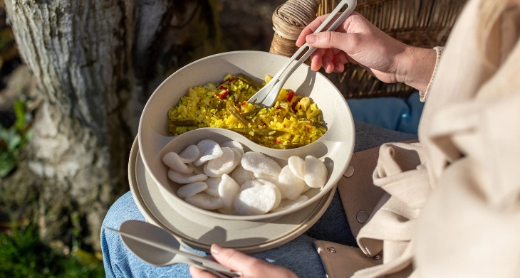 Lunchbox mit Reispfanne und Snackfächern beim Essen im Freien auf dem Schoß