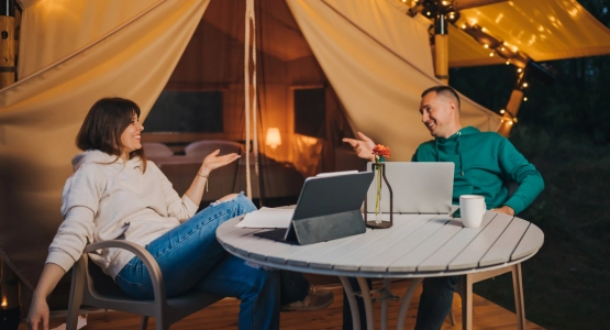Eine Frau und ein Mann sitzen an einem Campingtisch vor einem Zelt.