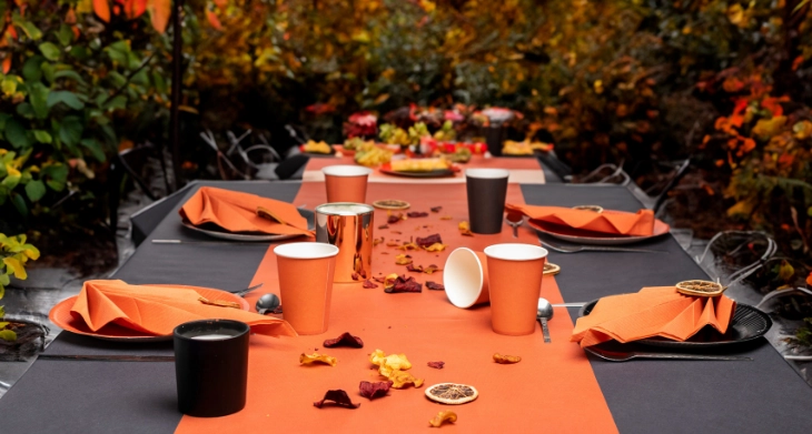 Herbstlich gedeckter Tisch mit orangem Einweggeschirr und Servietten im Freien.