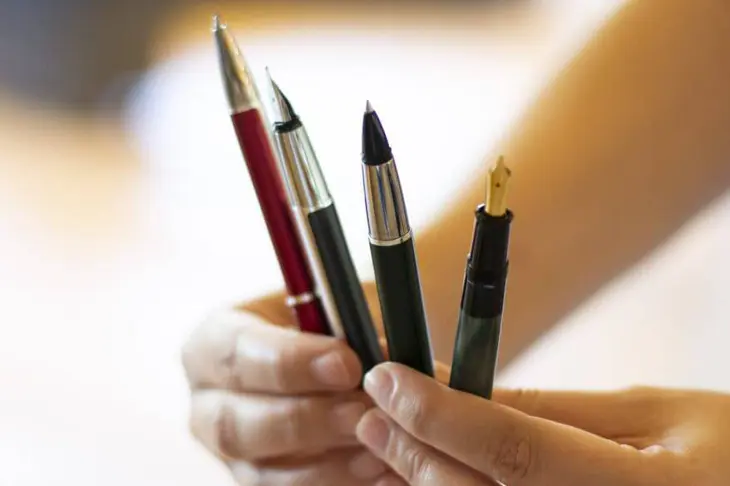 Eine Frau hält unterschiedliche Füller, Kugelschreiber und Tintenroller in den Händen.