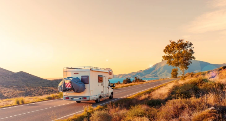 Wohnmobil fährt bei Sonnenuntergang auf leerer Straße durch Natur.