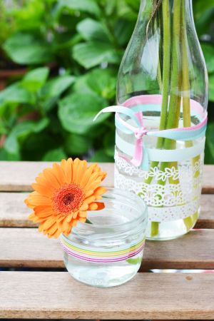 Flasche und Glas mit Maskingtape und bunten Bändern auf einem Balkontisch.