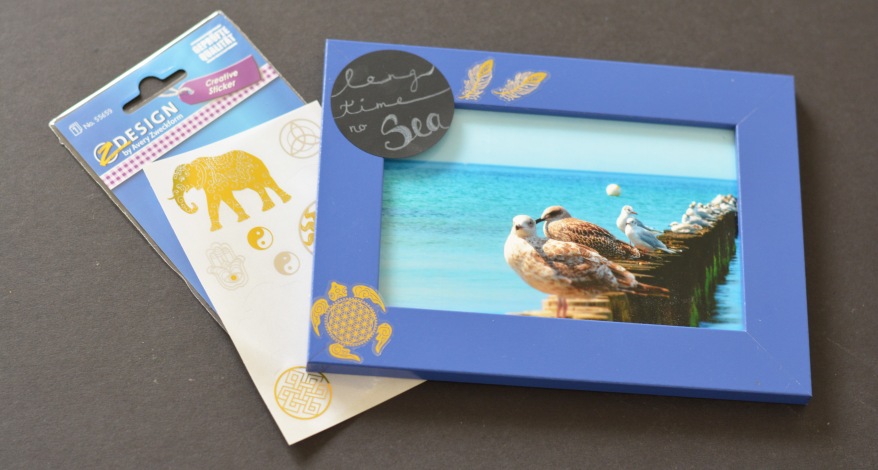 Blauer Rahmen mit Möwenbild, dekoriert mit goldenen Stickern, Stickerbogen liegen daneben