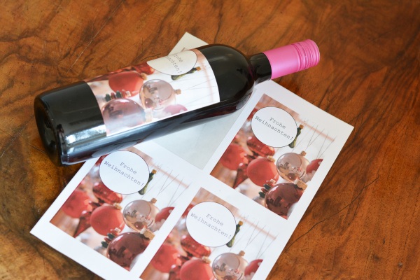 Flasche mit Weihnachtsetikett liegt neben bedruckten Etikettenbogen.