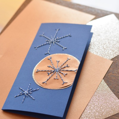 Blaue Karte mit drei gestickten Schneeflocken und Glitzerkreis