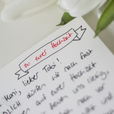 Nahaufnahme eines Ausschnitts einer handgeschriebenen Hochzeitskarte. In der rechte obenren Ecke ist eine Banderole gelettert, in der mit rotem Filzstift "zu eurer Hochzeit" steht.