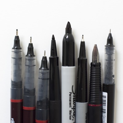 Verschiedene schwarze Stfite von rOtring und Sharpie mit verschiedenen Stiftspitzen liegen geöffnet auf einem weißen Untergrund.