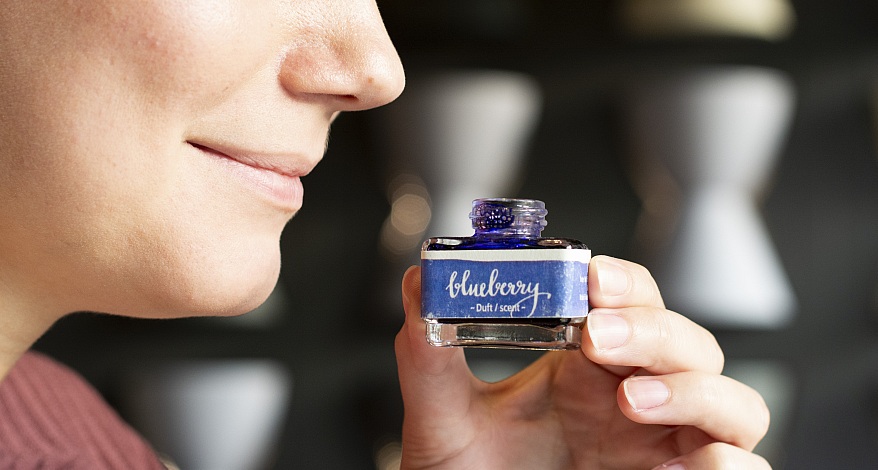 Person riecht an geöffneter Dufttinte mit „Blueberry“-Etikett.