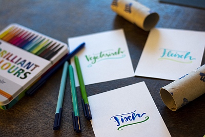 Beschriftete Zettel für Essensplanung neben Brushpens und Papprollen.