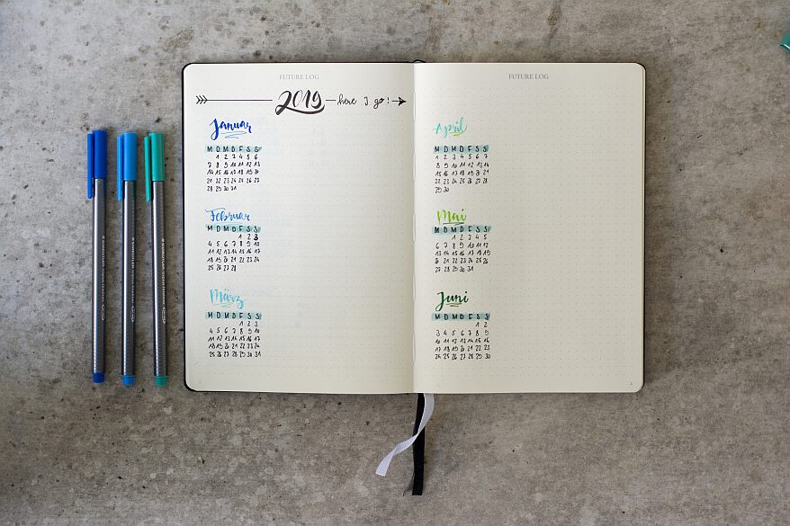 Offenes Notizbuch, in das ein Future Log für ein halbes Jahr zeigt. Daneben liegen 3 balue und tükise Fineliner.