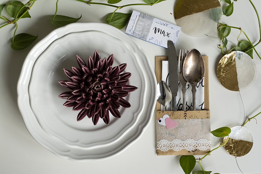Namenskärtchen, Bestecktasche und Blume auf gedecktem Tisch